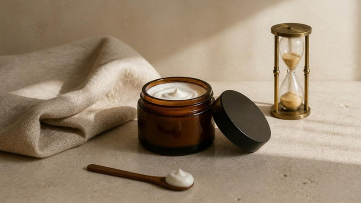 Pot de crème ouvert, petite spatule et linge en lin plié sur une tablette en pierre claire, article du Journal Calm&Co